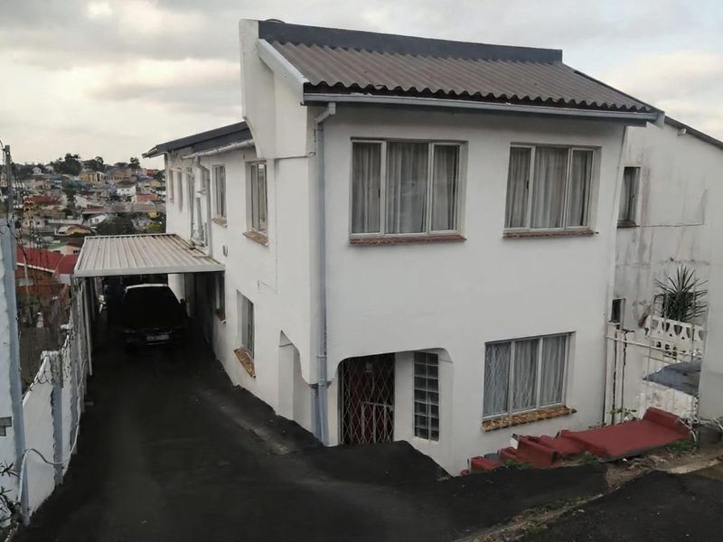 Two-story residential property featuring a corrugated metal roof, attached carport, and asphalt driveway, situated on a sloped lot.