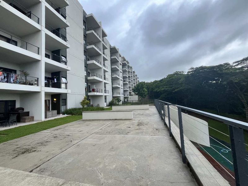 A spacious concrete patio area overlooking the apartment complex grounds, featuring metal balustrades and direct access to the building's rear facade.