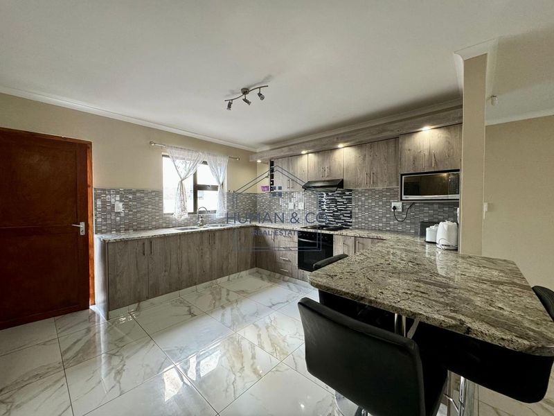 Modern kitchen featuring granite countertops, built-in appliances, tiled flooring, and ample cabinetry with integrated lighting.