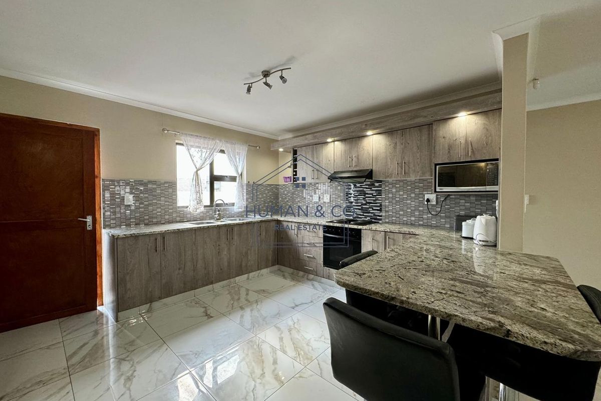 Modern kitchen featuring granite countertops, built-in appliances, tiled flooring, and ample cabinetry with integrated lighting.