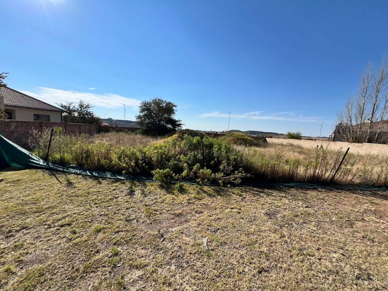 A vacant residential plot featuring natural grass, overgrown vegetation, and perimeter boundary walls, offering a blank canvas for future development.
