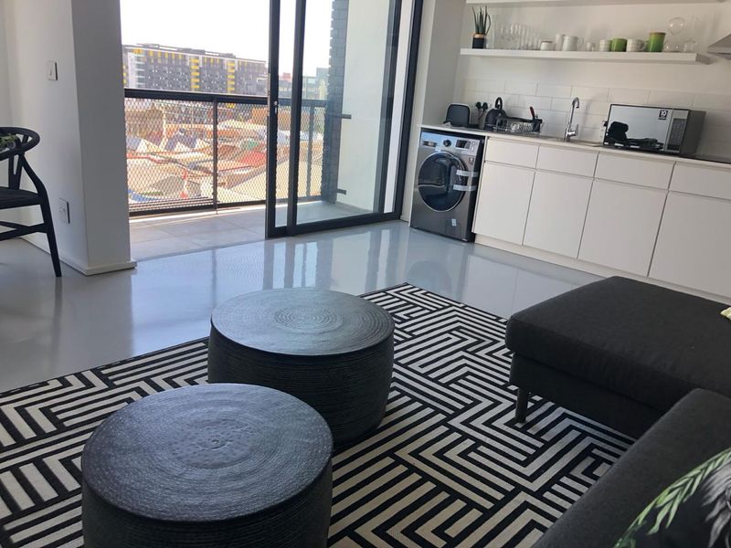 Modern open-plan living area featuring a compact kitchenette with white cabinetry, subway tile backsplash, and direct access to a private balcony.
