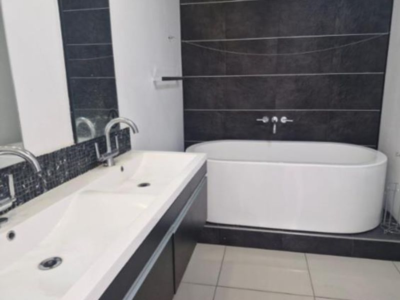 Modern bathroom featuring a double vanity with integrated sinks and a sleek freestanding bathtub set against a dark tiled feature wall.