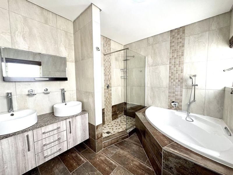 Modern bathroom featuring a double vanity with vessel sinks, a glass-enclosed walk-in shower, and a built-in corner bathtub with tiled surround.