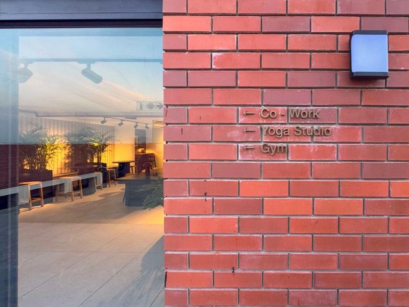 Exterior view of a modern brick building facade featuring directional signage for communal facilities including a co-working space, yoga studio, and gym.