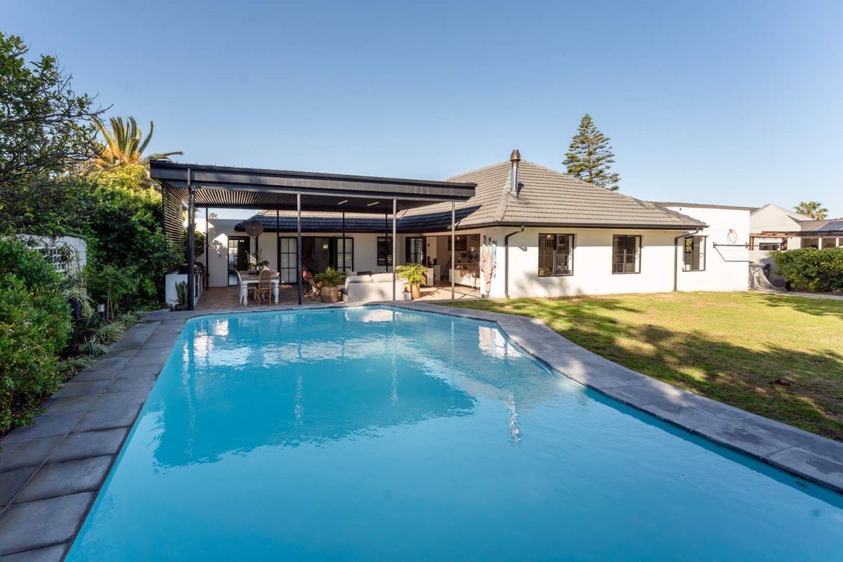 Rear view of the property featuring a well-maintained swimming pool, a spacious covered patio area, and a landscaped garden with lawn.