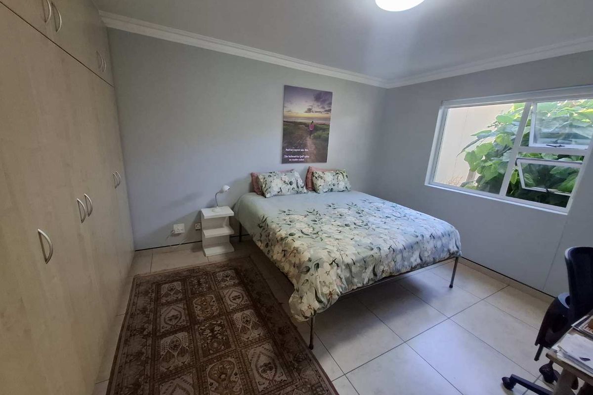 A well-maintained bedroom featuring neutral tiled flooring, ample built-in cupboard storage, and a large window providing natural light.