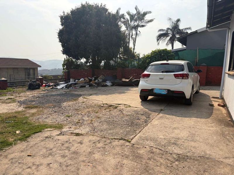 Rear exterior area featuring a concrete driveway and brick boundary wall, currently showing significant surface wear and accumulation of debris.