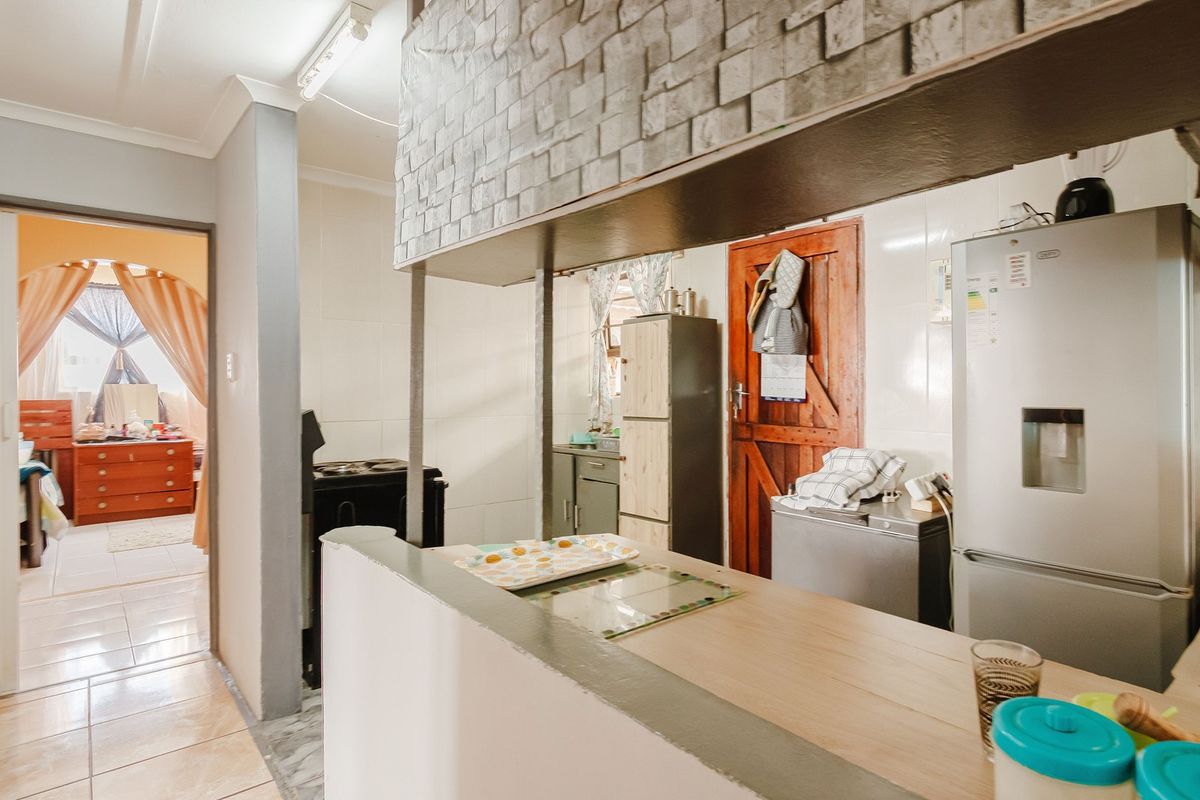 A functional kitchen featuring a breakfast bar, tiled splashback, and a distinctive stone-look bulkhead, offering potential for a modern cosmetic update.