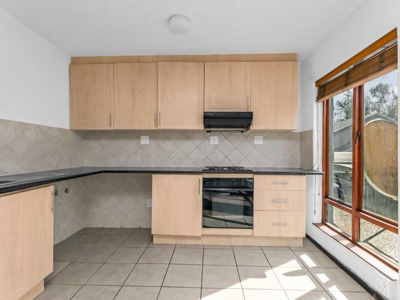 A functional kitchen featuring light wood cabinetry, dark countertops, built-in oven and hob, tiled backsplash, and large window providing natural light.