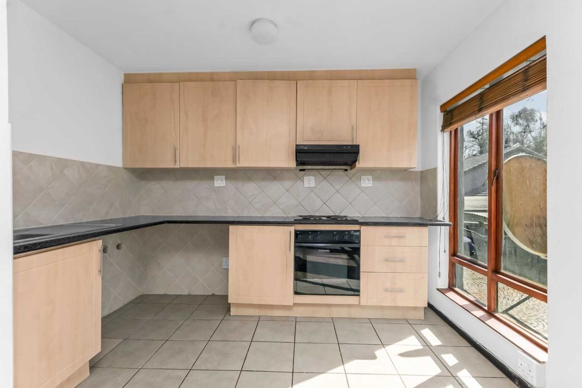 A functional kitchen featuring light wood cabinetry, dark countertops, built-in oven and hob, tiled backsplash, and large window providing natural light.