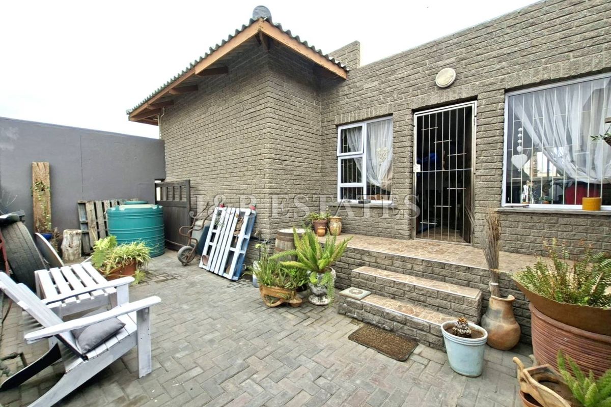 A rear exterior view of the property featuring a paved patio area, brick facade, and a secure entrance with a metal security gate.