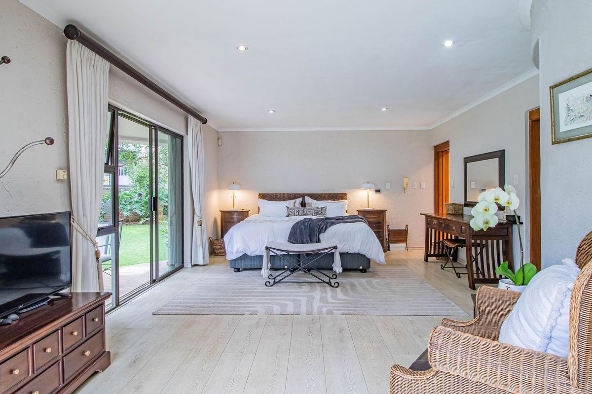 Spacious bedroom featuring light wood-look flooring, recessed downlighting, and large sliding glass doors providing direct access to the garden.