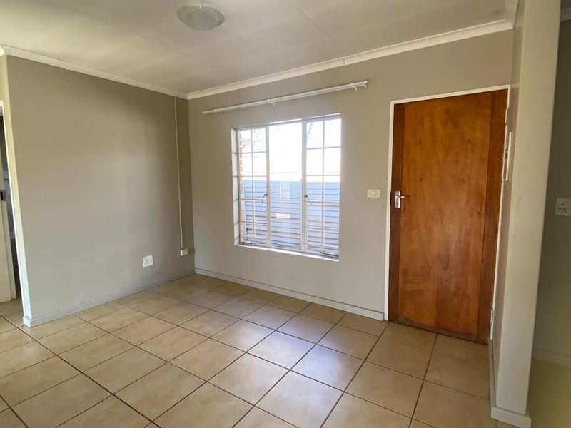 An empty living room featuring neutral wall paint, tiled flooring, a window with security bars, and a wooden door.