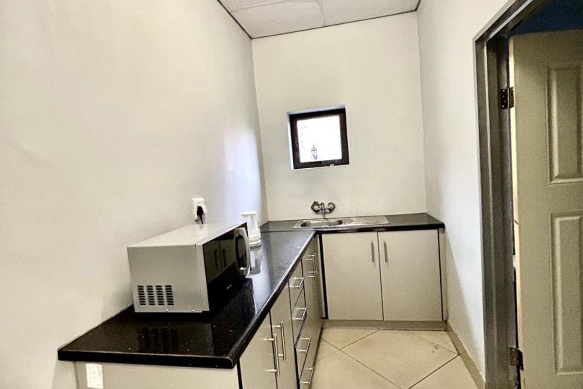 A compact office kitchenette featuring dark granite countertops, light-toned cabinetry, a stainless steel sink, and a drop ceiling.