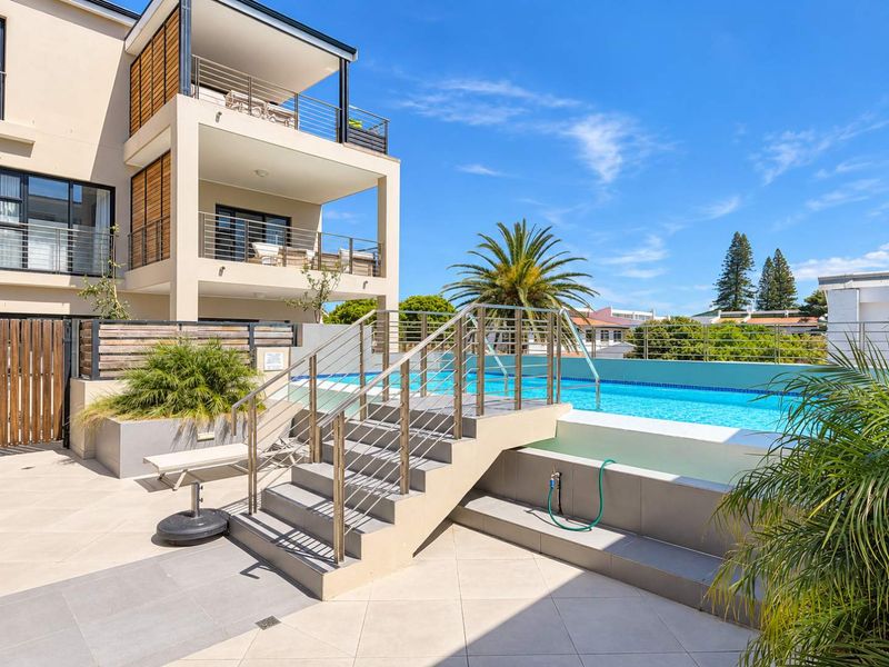 A well-maintained outdoor pool area featuring a raised swimming pool, modern stainless steel railings, and a concrete staircase set within a tiled patio space.