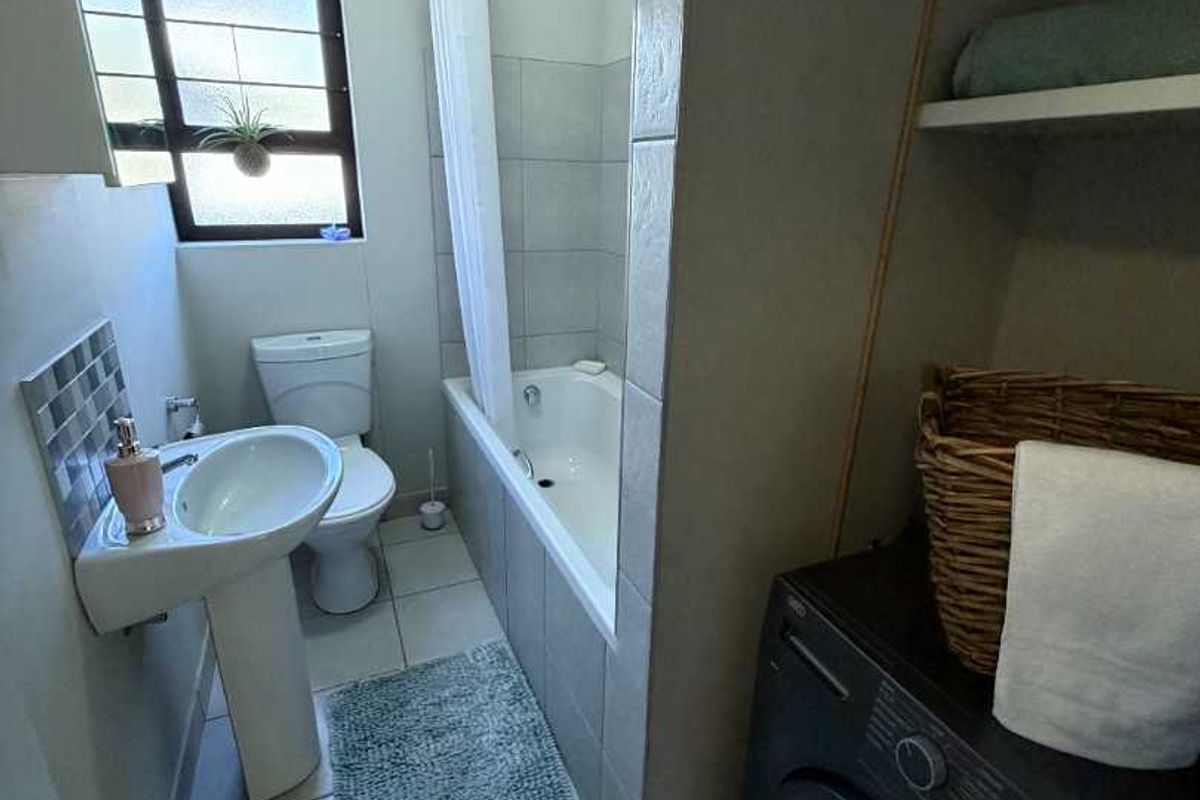 A functional bathroom featuring a pedestal basin, toilet, and a bathtub with shower attachment, complemented by tiled flooring and convenient built-in storage shelving.
