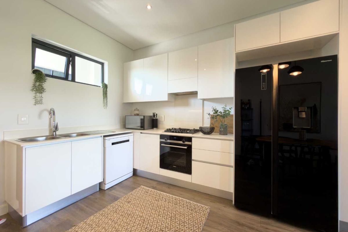 Modern kitchen featuring white gloss cabinetry, integrated oven, gas hob, extractor fan, double sink, and space for a large refrigerator.