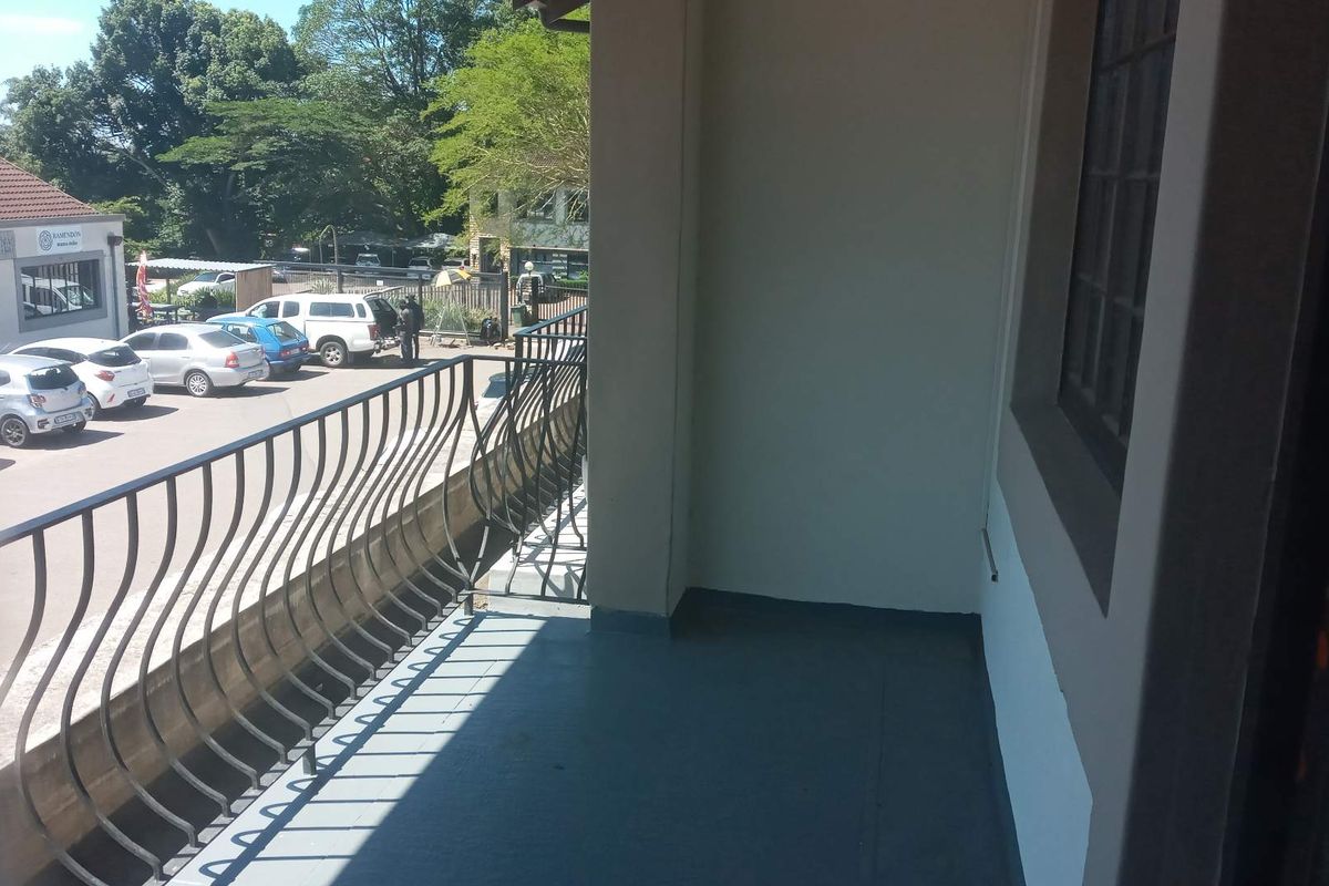 A covered balcony area featuring a decorative metal balustrade and painted concrete flooring, overlooking the office parking area.