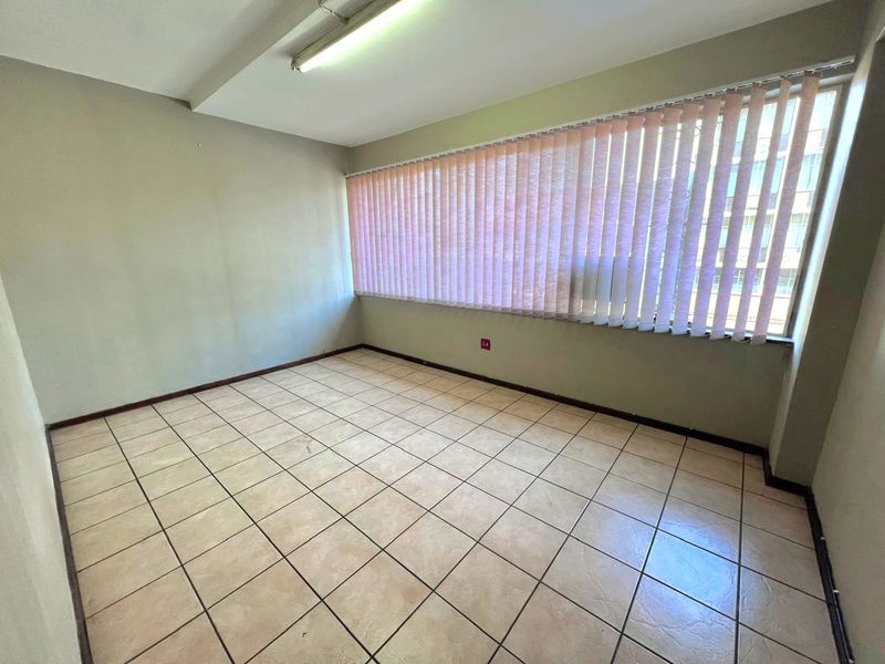 An empty office space featuring ceramic floor tiles, large windows with vertical blinds, and overhead fluorescent lighting.