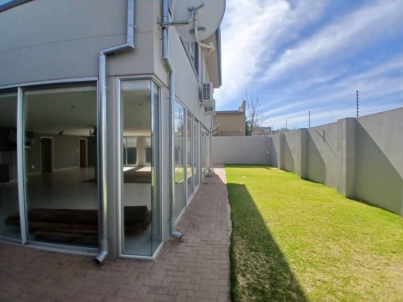 Rear exterior view featuring a paved walkway, manicured lawn, perimeter wall, and large sliding glass doors providing access to the interior living space.