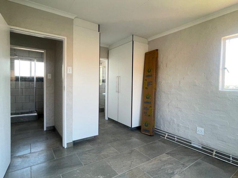 A bright, empty bedroom featuring neutral tiled flooring, built-in cupboards, and access to an adjoining bathroom.