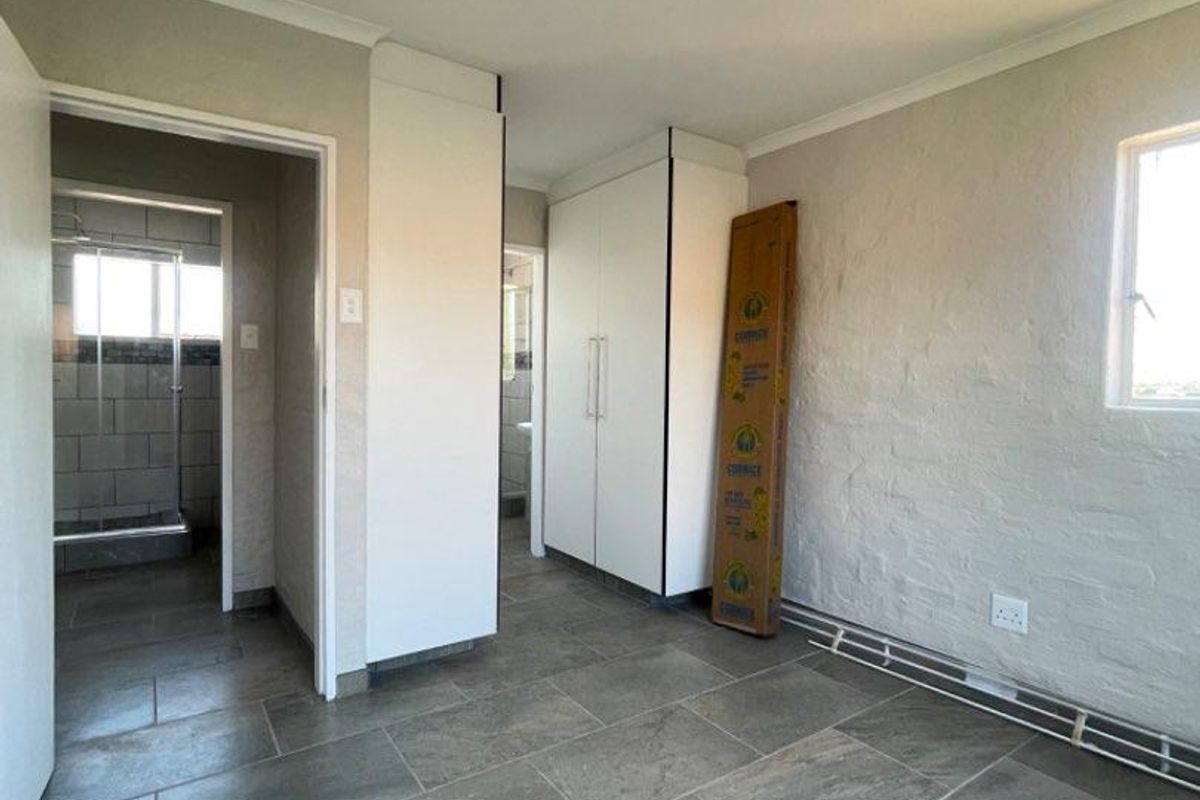 A bright, empty bedroom featuring neutral tiled flooring, built-in cupboards, and access to an adjoining bathroom.