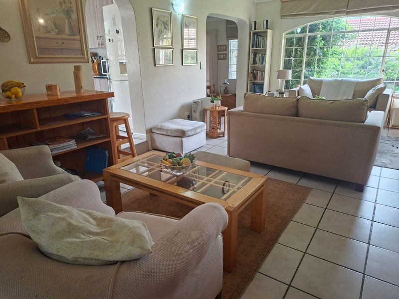 Open plan living area featuring tiled flooring, an arched doorway leading to the kitchen, and a large arched window providing natural light.