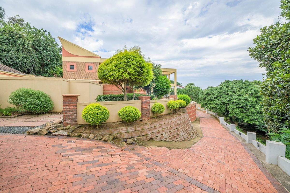 Rear exterior view featuring a brick paved driveway, tiered retaining walls, and established garden landscaping surrounding the property structure.