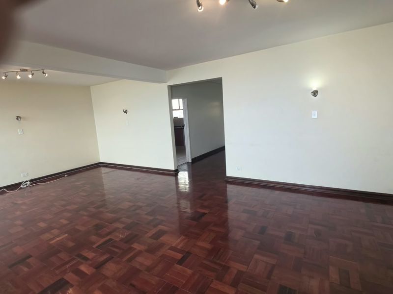 Spacious, empty living area featuring well-maintained parquet flooring, neutral walls, and modern ceiling and wall lighting fixtures.