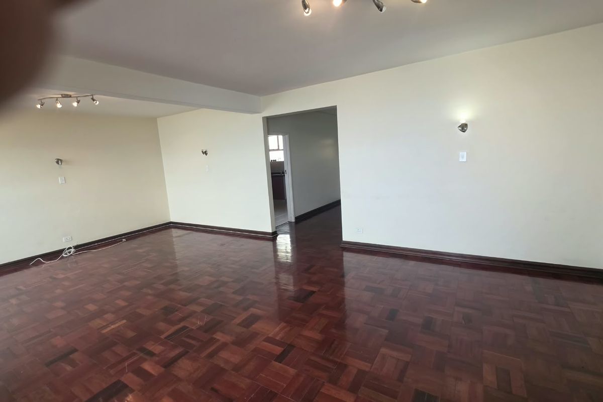Spacious, empty living area featuring well-maintained parquet flooring, neutral walls, and modern ceiling and wall lighting fixtures.