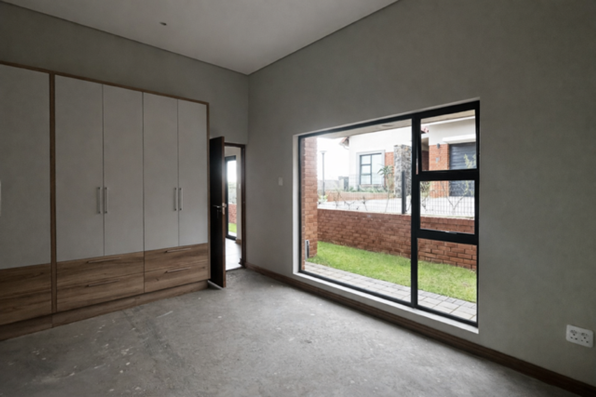 A bright bedroom featuring built-in wooden cabinetry, large windows with garden views, and a neutral interior finish.