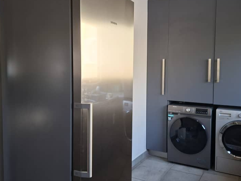 A functional laundry area featuring modern grey built-in cabinetry and tiled flooring, designed for efficient appliance integration.