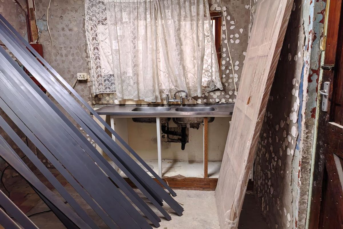 A kitchen in need of significant renovation, featuring a double stainless steel sink and damaged wall surfaces requiring repair and modernization.