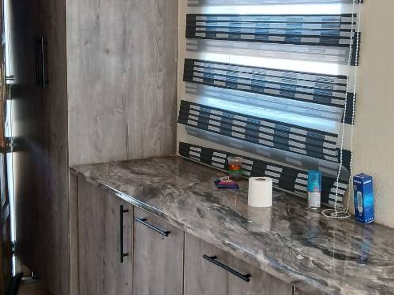 A functional scullery or utility area featuring modern wood-look cabinetry, marble-effect laminate countertops, and tiled flooring.