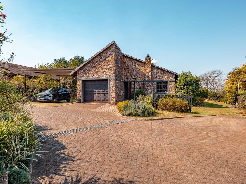Front elevation of a stone-clad townhouse featuring a paved driveway, single garage, and attached carport in a well-maintained setting.