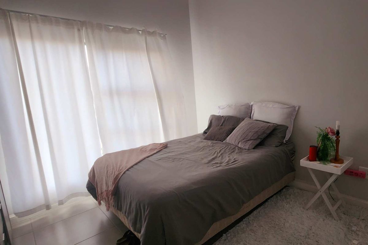 A bedroom featuring tiled flooring and a large window with curtains, providing natural light to the space.