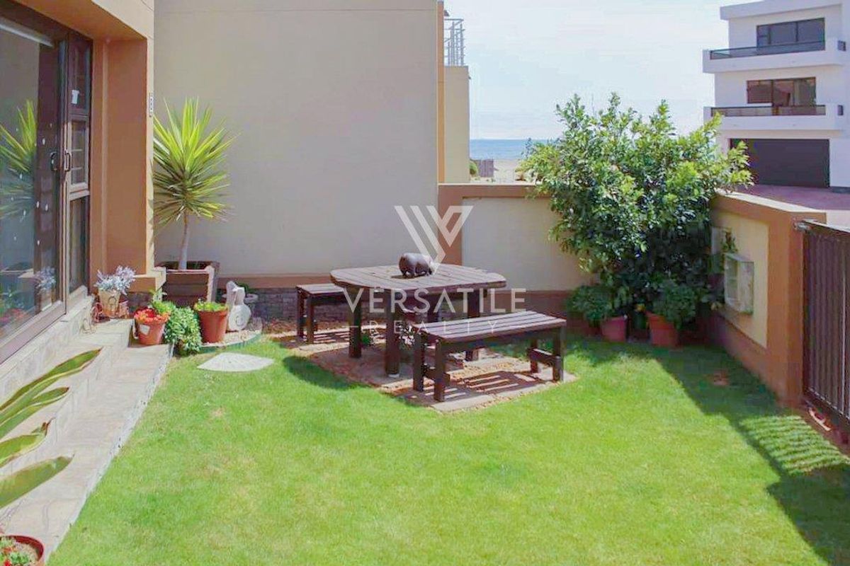 A private rear garden featuring a well-maintained lawn, paved patio area, and direct access to the interior via sliding glass doors.