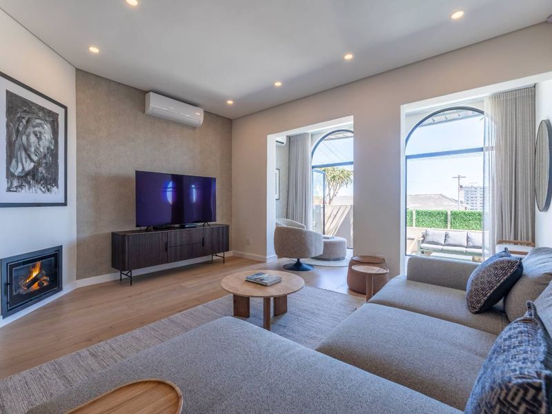Modern living room featuring timber flooring, a built-in fireplace, split-system air conditioning, and large arched windows providing natural light and access to the balcony.