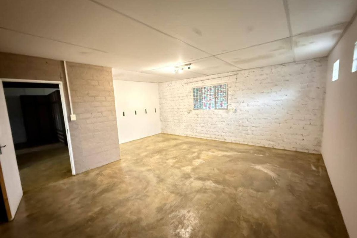 An empty, versatile living space featuring exposed brick walls, polished concrete flooring, and a drop ceiling, offering a blank canvas for renovation.