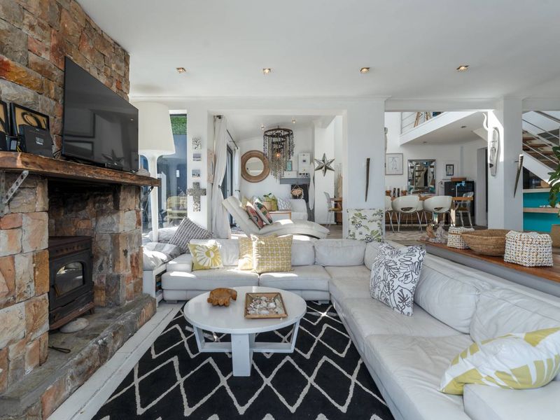 Spacious open-plan living area featuring a prominent stone fireplace with a wood-burning stove, recessed lighting, and an integrated staircase.