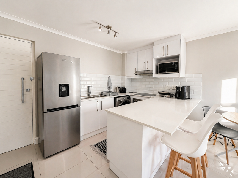 Modern kitchen featuring white cabinetry, subway tile backsplash, quartz countertops, and integrated appliances, including a breakfast bar area.