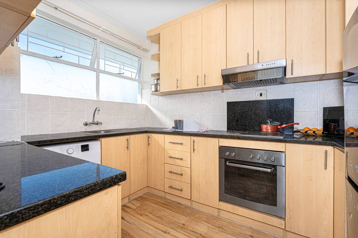 Functional kitchen featuring light wood cabinetry, dark granite countertops, built-in oven, extractor fan, and tiled backsplash with ample natural light.