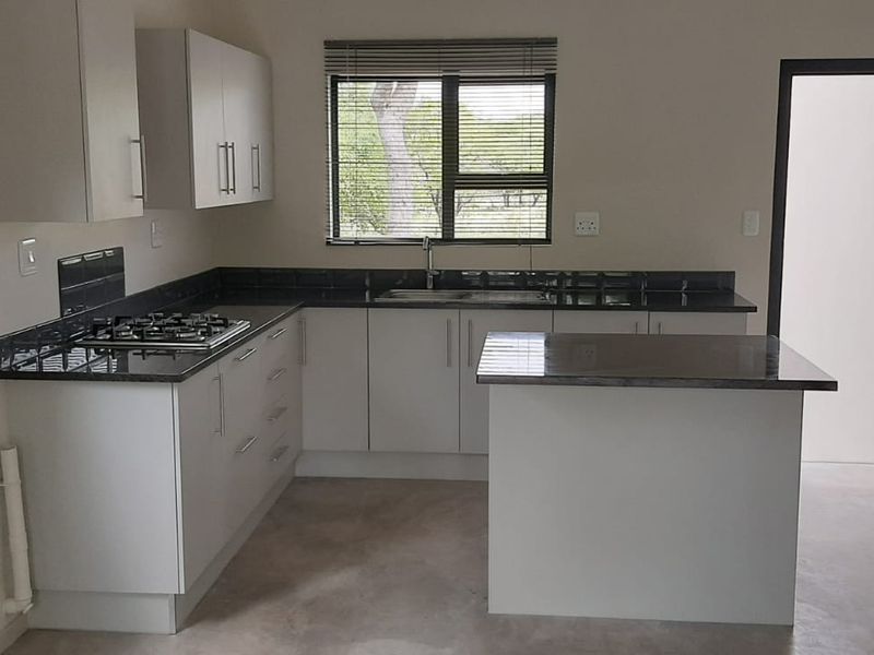 A modern, clean kitchen featuring white cabinetry, dark stone countertops, a gas hob, and a central island, offering a functional and bright workspace.