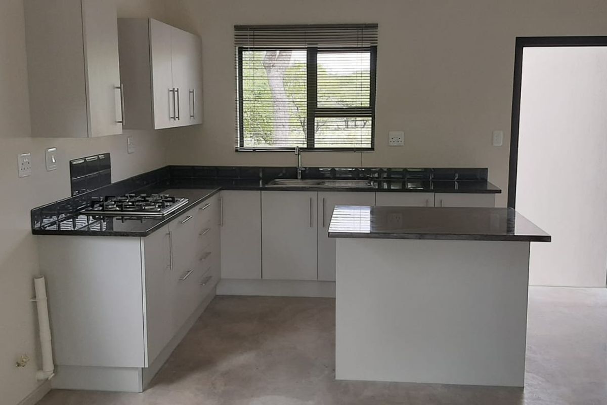 A modern, clean kitchen featuring white cabinetry, dark stone countertops, a gas hob, and a central island, offering a functional and bright workspace.