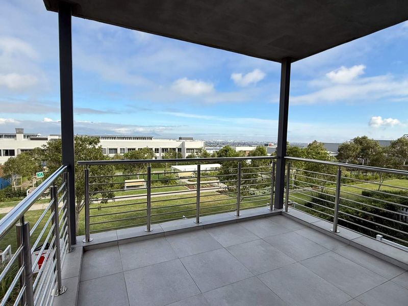 A spacious covered balcony featuring modern tiled flooring and a stainless steel balustrade, offering elevated views over the retirement village grounds.