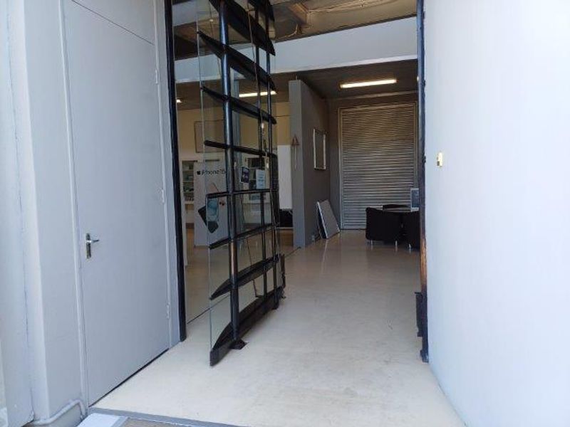 Entrance area featuring a modern pivot glass door, exposed industrial-style ceiling, and a secure roller shutter door leading into the office space.