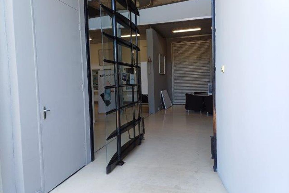 Entrance area featuring a modern pivot glass door, exposed industrial-style ceiling, and a secure roller shutter door leading into the office space.