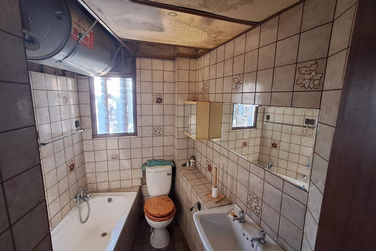 A dated bathroom featuring a bathtub, pedestal sink, and toilet, with visible signs of ceiling water damage and aged wall tiling.