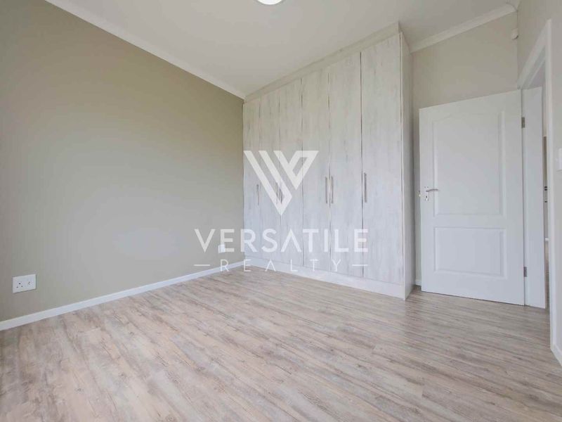 A clean, empty bedroom featuring light-toned laminate flooring and modern built-in cupboards with a neutral wall finish.